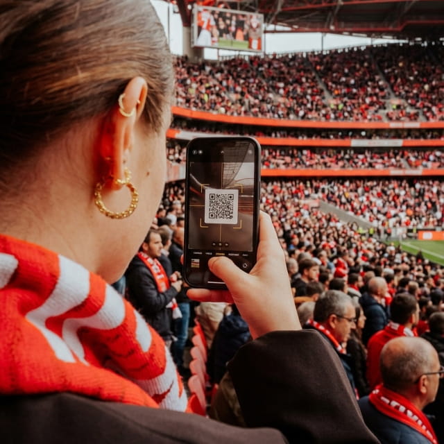 A fan in the stands scanning a QR code on their phone to join the game